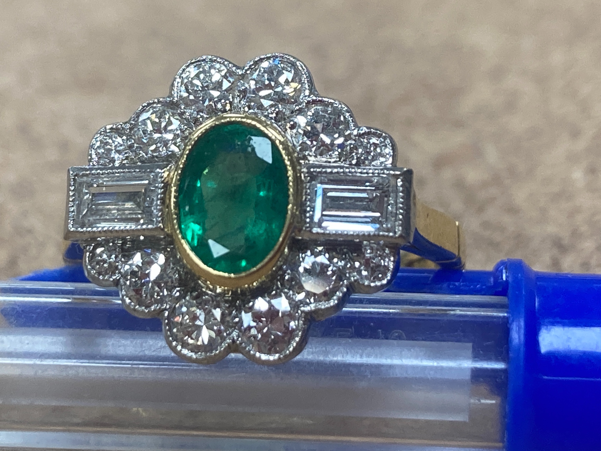 A modern 18ct gold, emerald, baguette and round cut diamond set shaped oval cluster ring, size L/M, gross weight 4.4 grams.